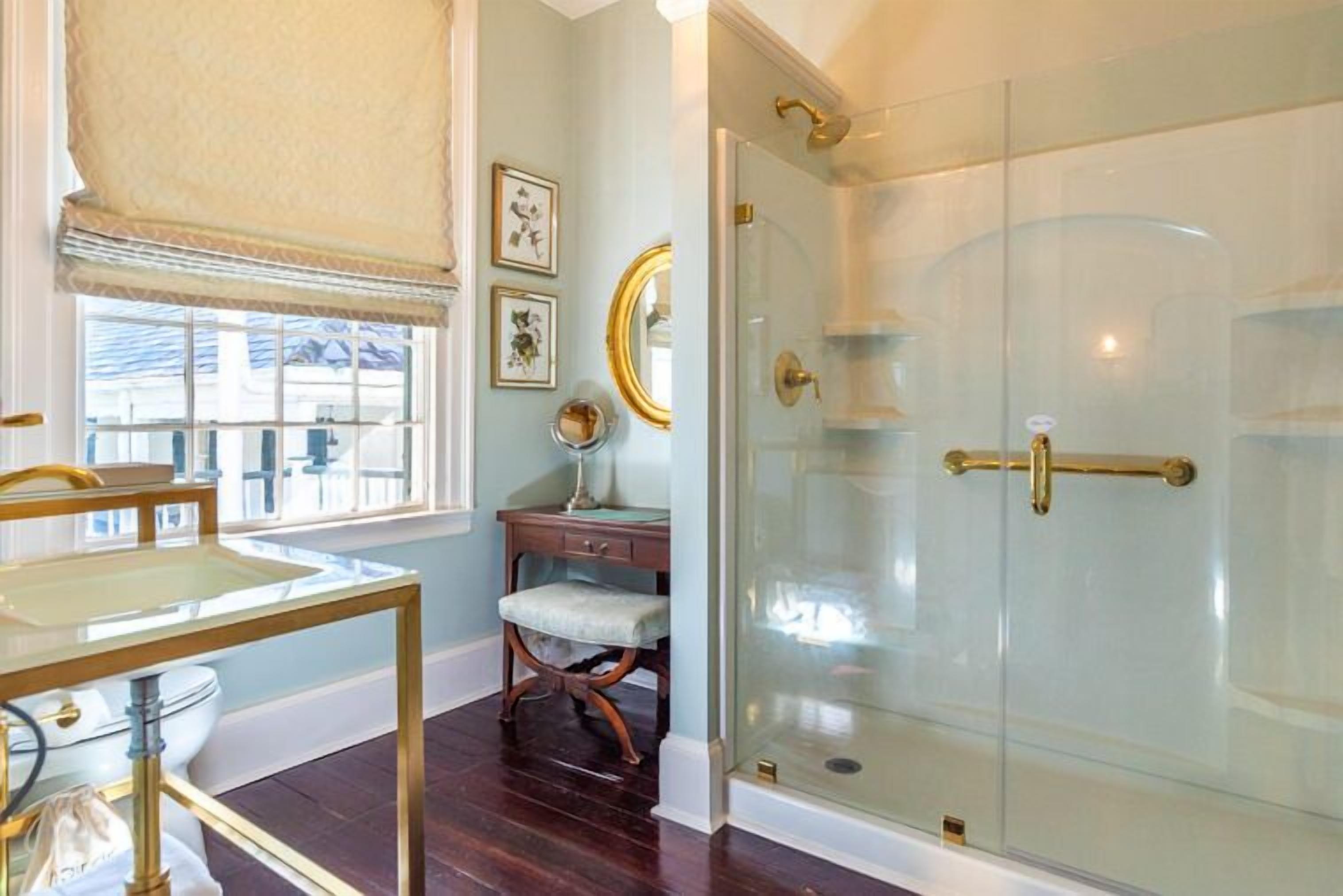 A bathroom with a glass-enclosed shower, a vanity with a mirror, and a window with a view of the outside.