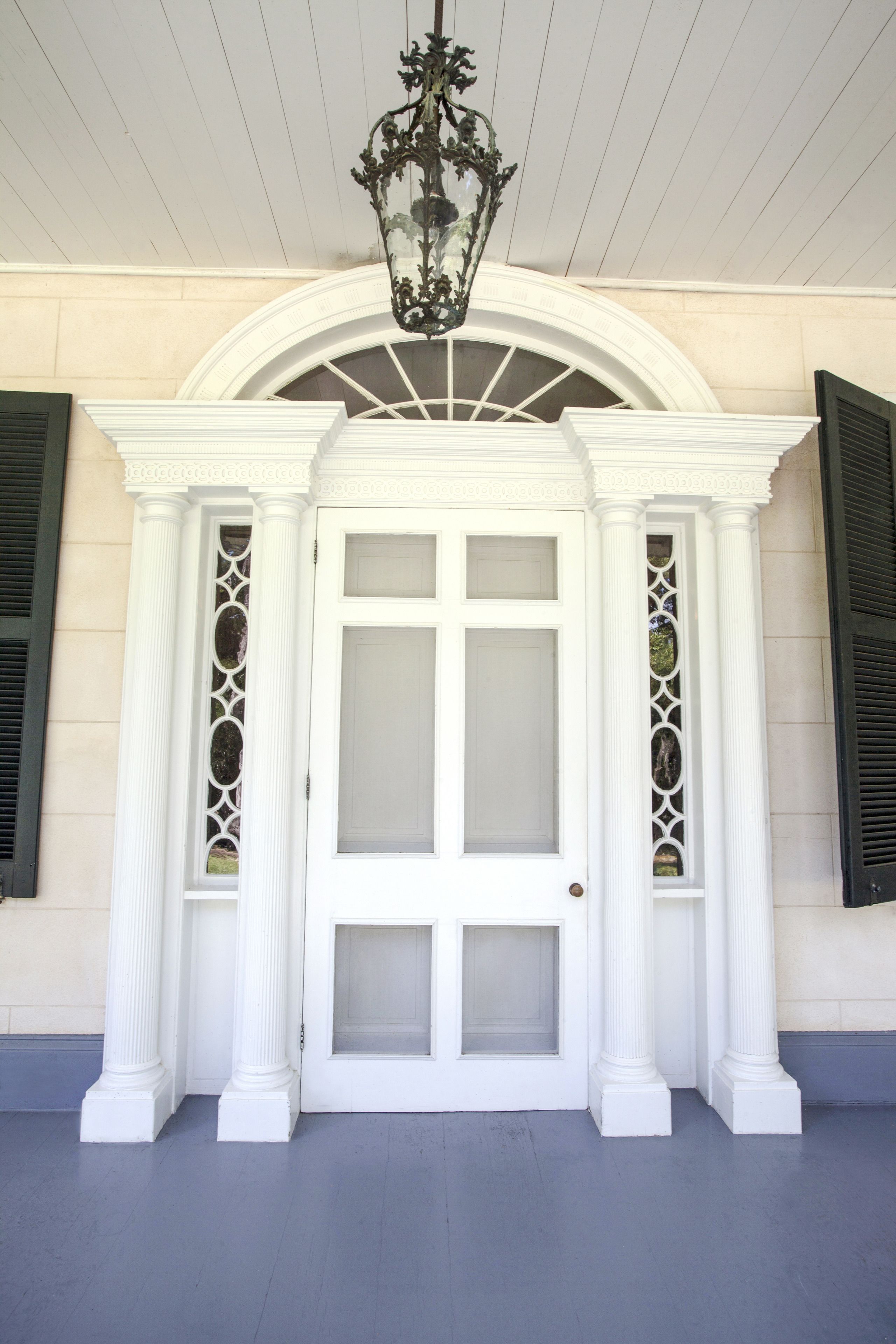 A white door with a glass panel, flanked by white columns and a decorative ceiling light.