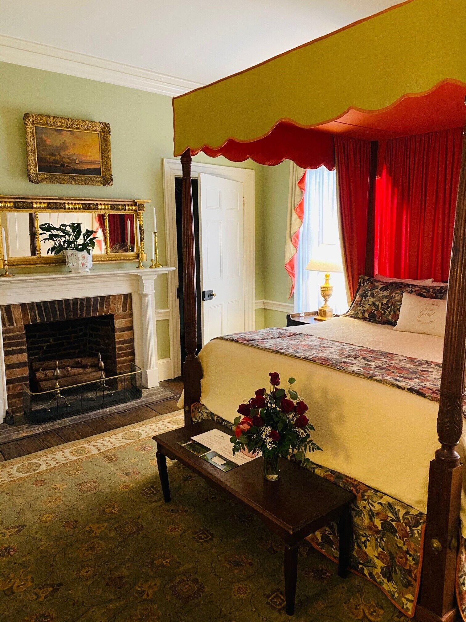 A four-poster bed with a floral bedspread, a fireplace with a mantel, and a painting on the wall.