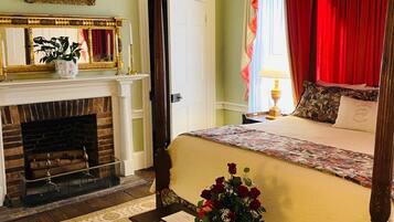 A four-poster bed with a floral bedspread, a fireplace with a mantel, and a painting on the wall.