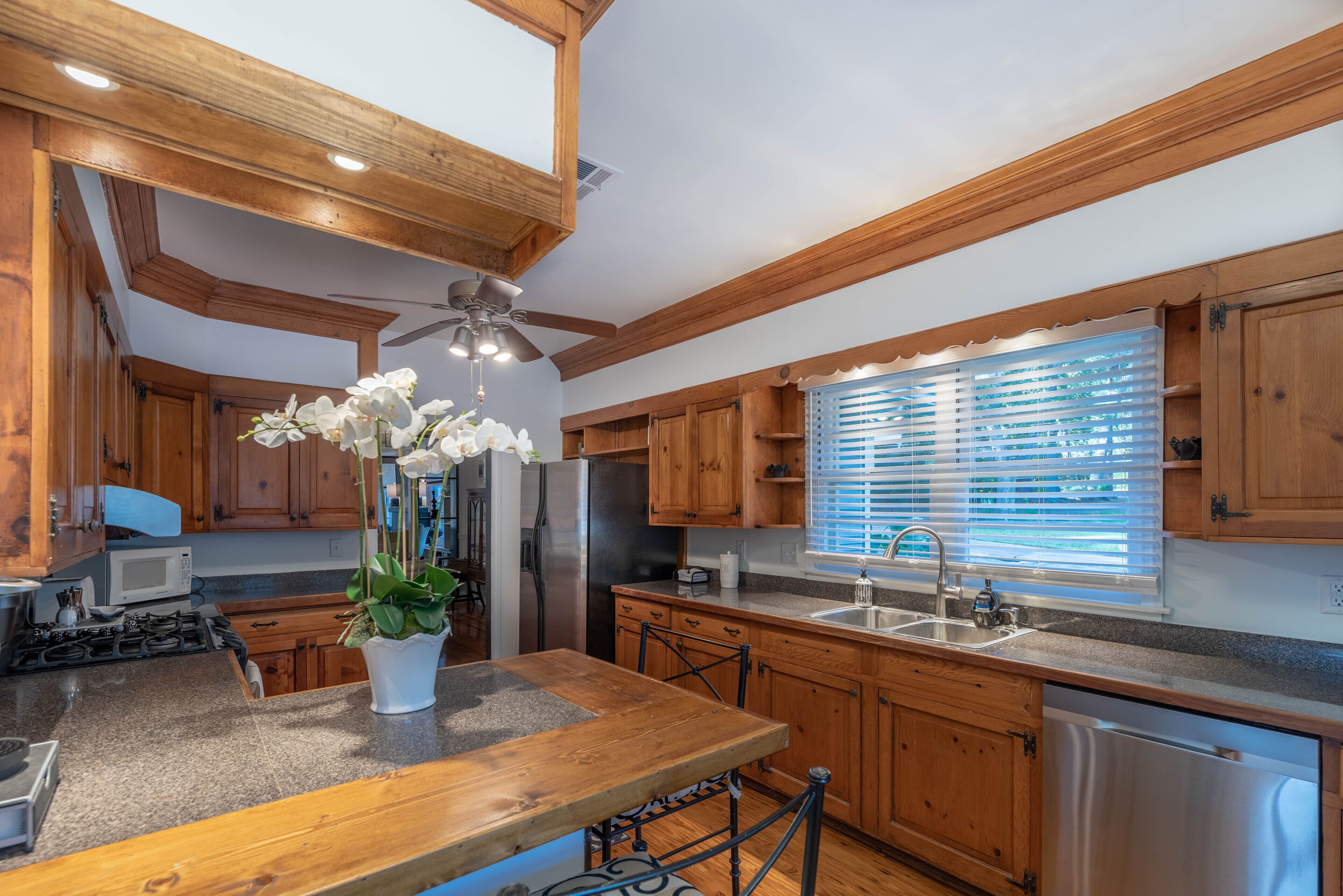 A kitchen with wooden cabinets, a granite countertop, a stainless steel refrigerator, and a ceiling fan.