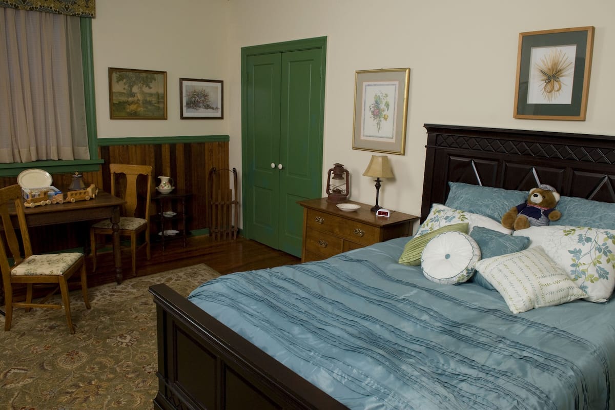 Une chambre à coucher avec un lit, un bureau, une chaise, une commode et une porte verte.