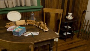 A wooden dining table with a toy train set, a plate, and a pitcher on a matching side table. - The Tinder Guest House (Ashland)
