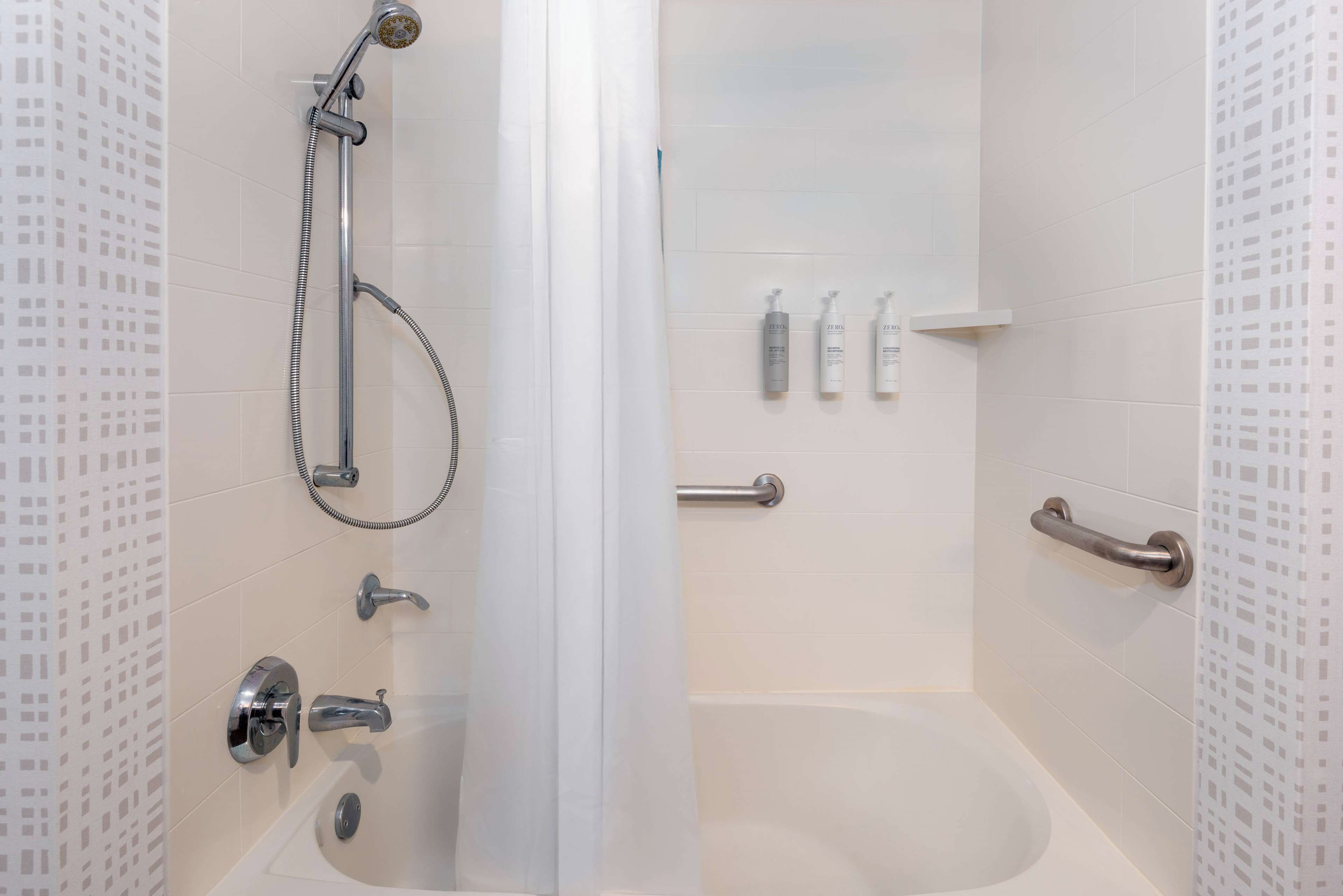 A bathroom with a bathtub, shower, and handrails.