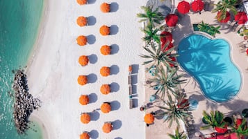 Vista aérea de una playa con arena blanca, piscina y numerosos sombrillas naranjas.