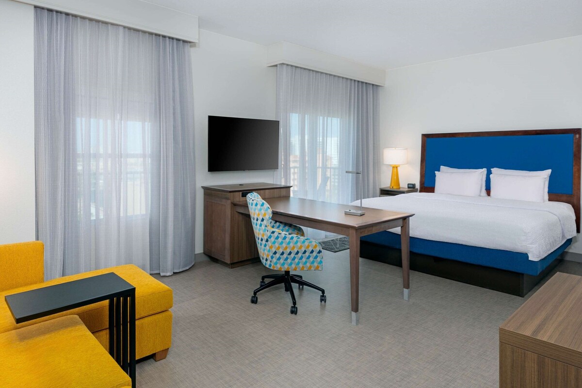Ein Hotelzimmer mit Bett, Schreibtisch, Stuhl, Fernseher und Vorhängen.