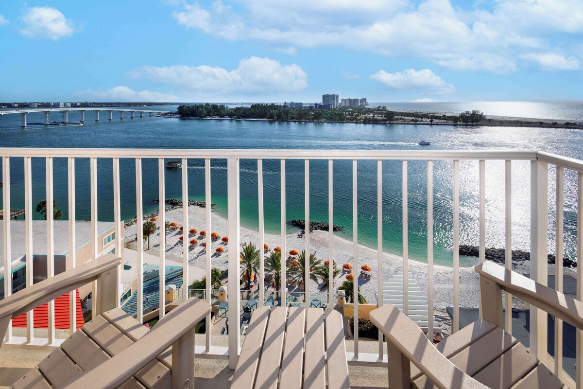 Ein Balkon mit Blick auf einen Strand, ein Pool und eine Brücke in der Ferne.