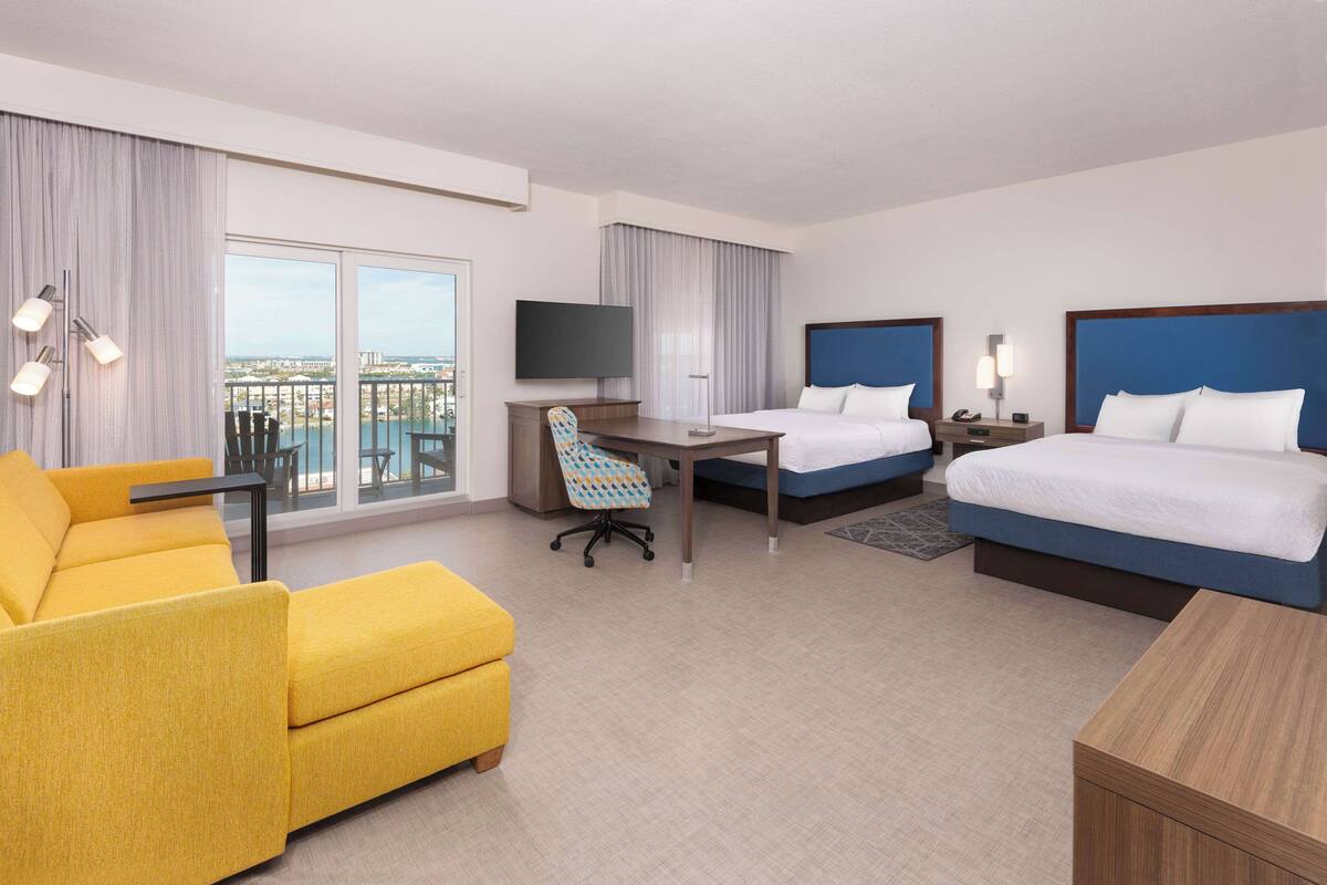 A hotel room with two beds, a desk, a chair, a TV, and a sofa.