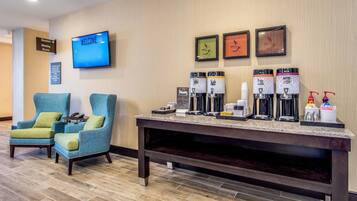 Vestíbulo de hotel con recepción, máquinas de café, televisor mostrando 'BIENVENIDOS' y zona de estar con sillas.
