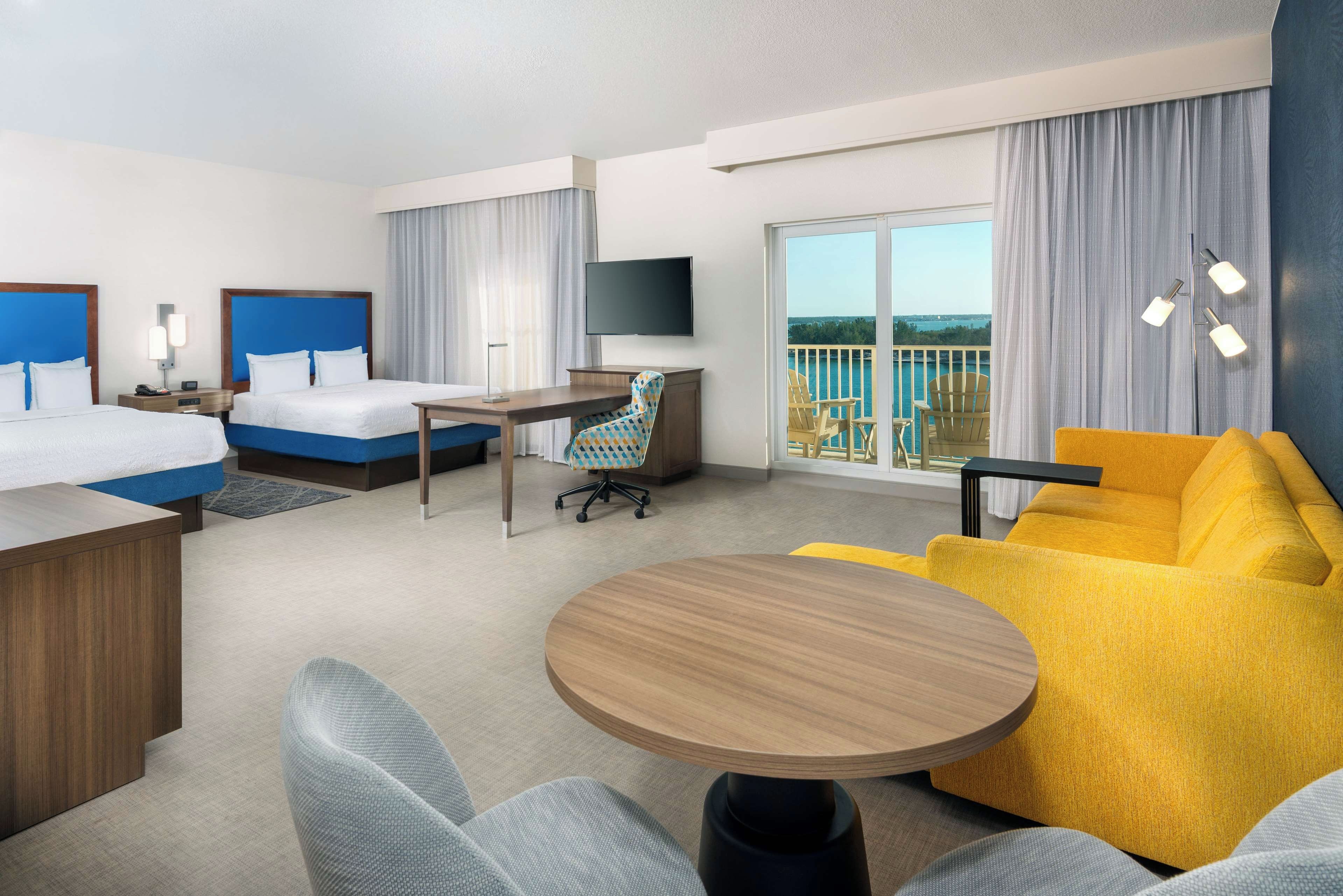 A hotel room with two beds, a desk, a round table, a sofa, and a TV.