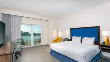Quarto de hotel com cama, escrivaninha, cadeira, mesa de cabeceira e vista para o mar.