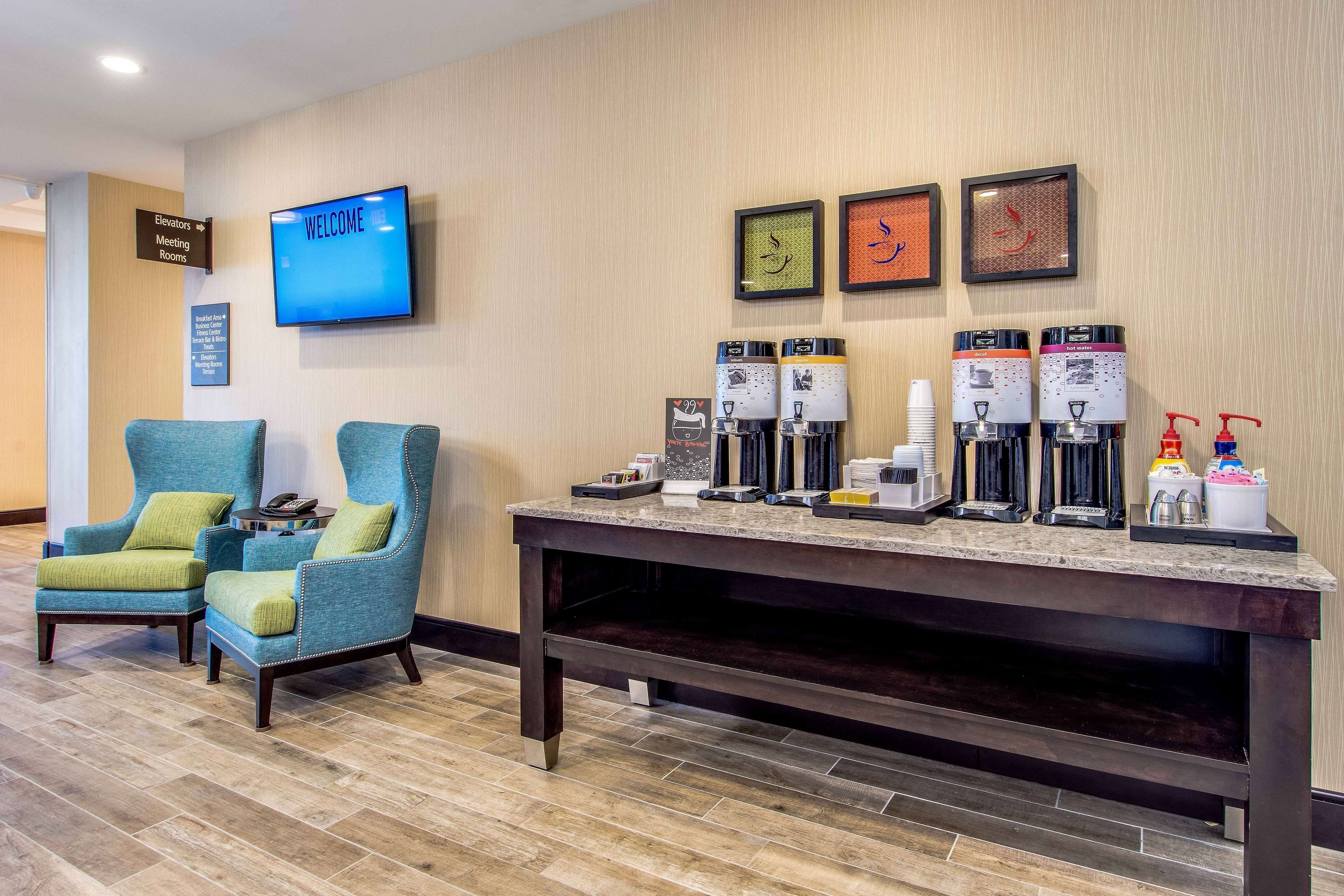 A hotel lobby with a reception desk, coffee machines, and seating area.