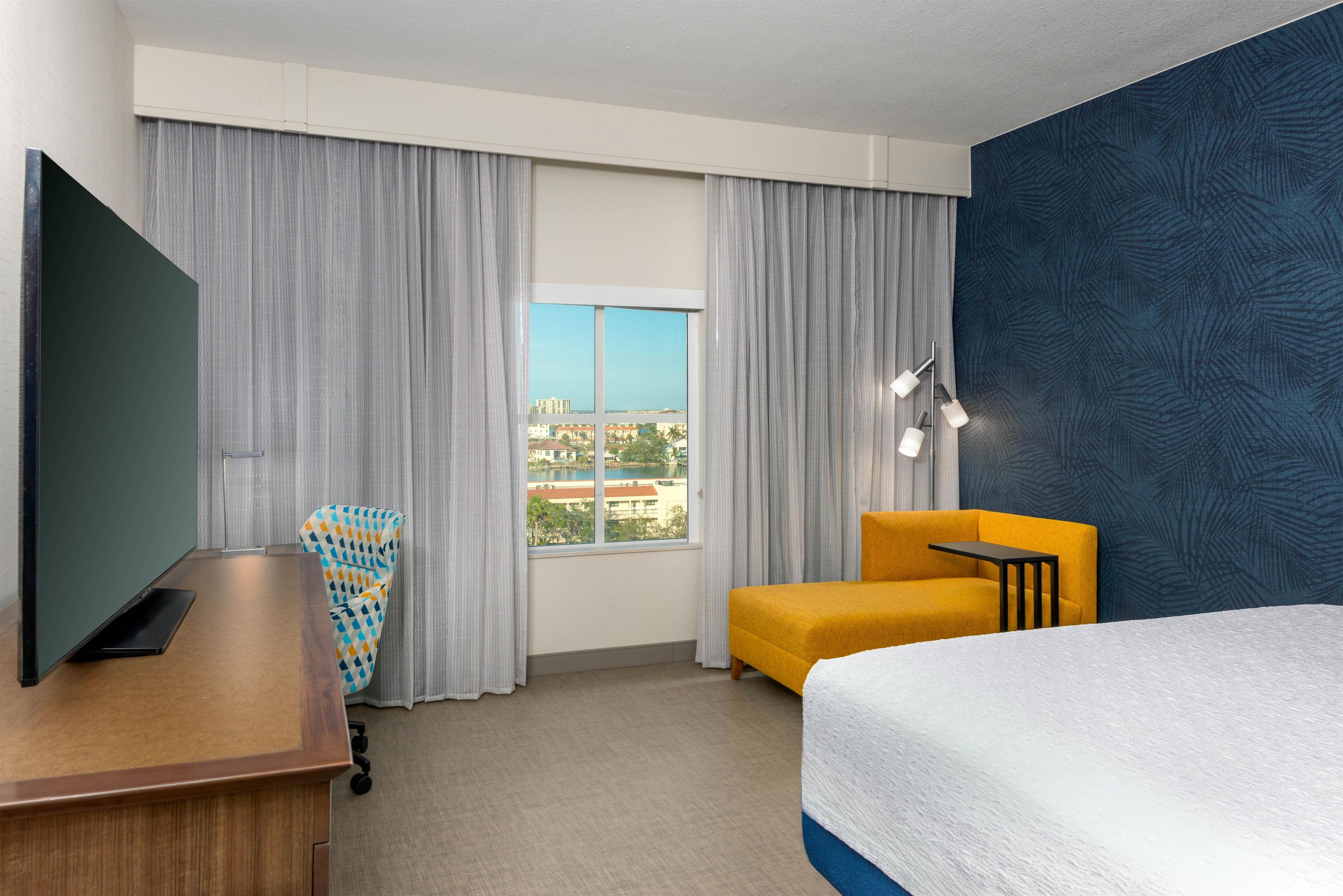Une chambre d’hôtel équipée d’un lit, d’un bureau, d’une chaise et d’une grande fenêtre donnant sur la ville.