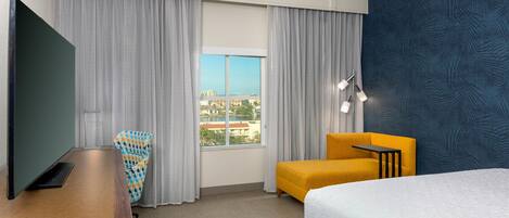 Une chambre d’hôtel équipée d’un lit, d’un bureau, d’une chaise et d’une grande fenêtre donnant sur la ville.