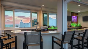 A bar area with a counter, bar stools, and a view of the sunset through large windows.