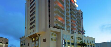 Un hotel de varios pisos con fachada plana, múltiples balcones y una señalización destacada que indica que es un establecimiento Hampton Inn & Suites.