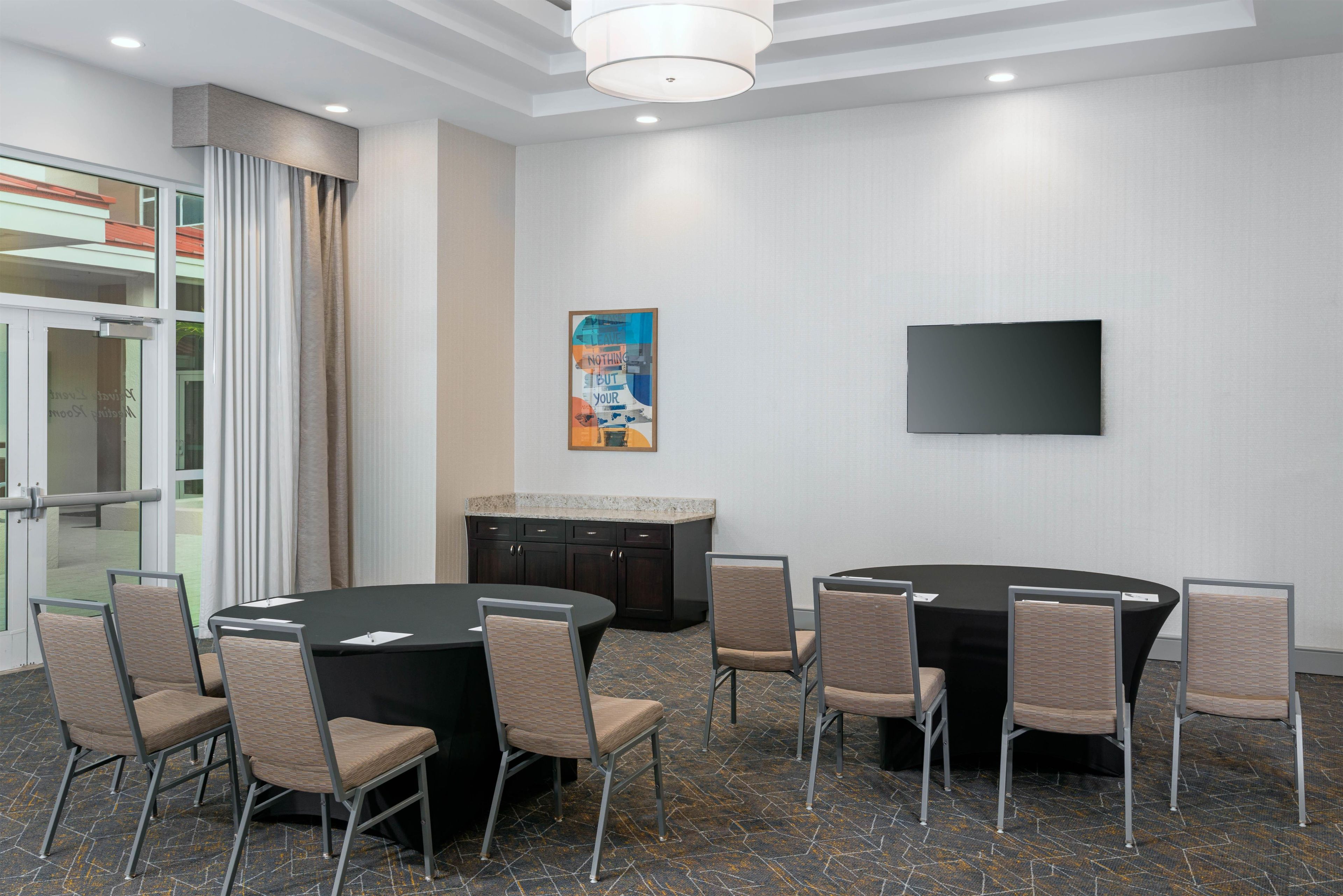 A conference room with a round table, chairs, a television, and a painting on the wall.