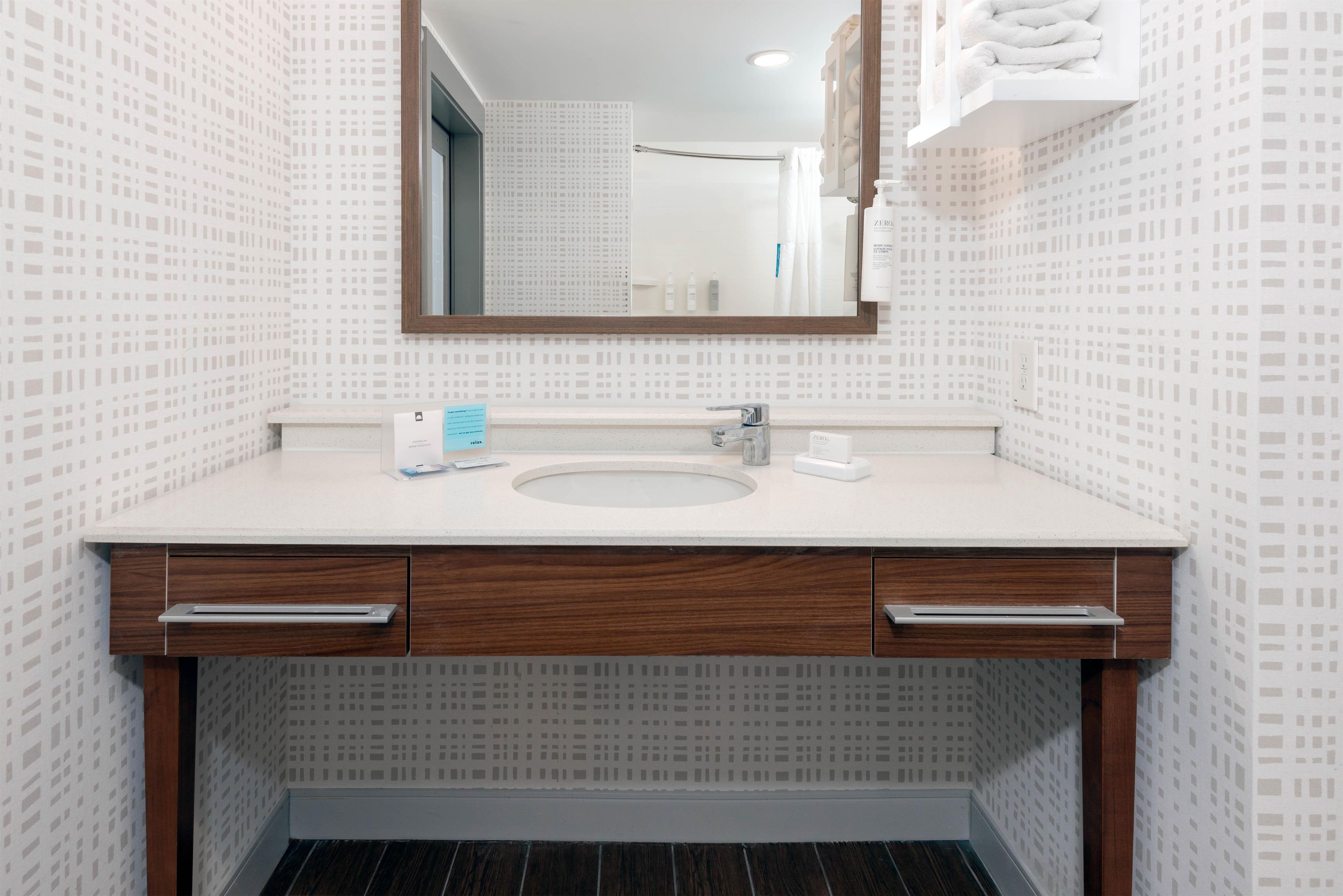A modern bathroom with a white sink, wooden cabinetry, and a mirror above.
