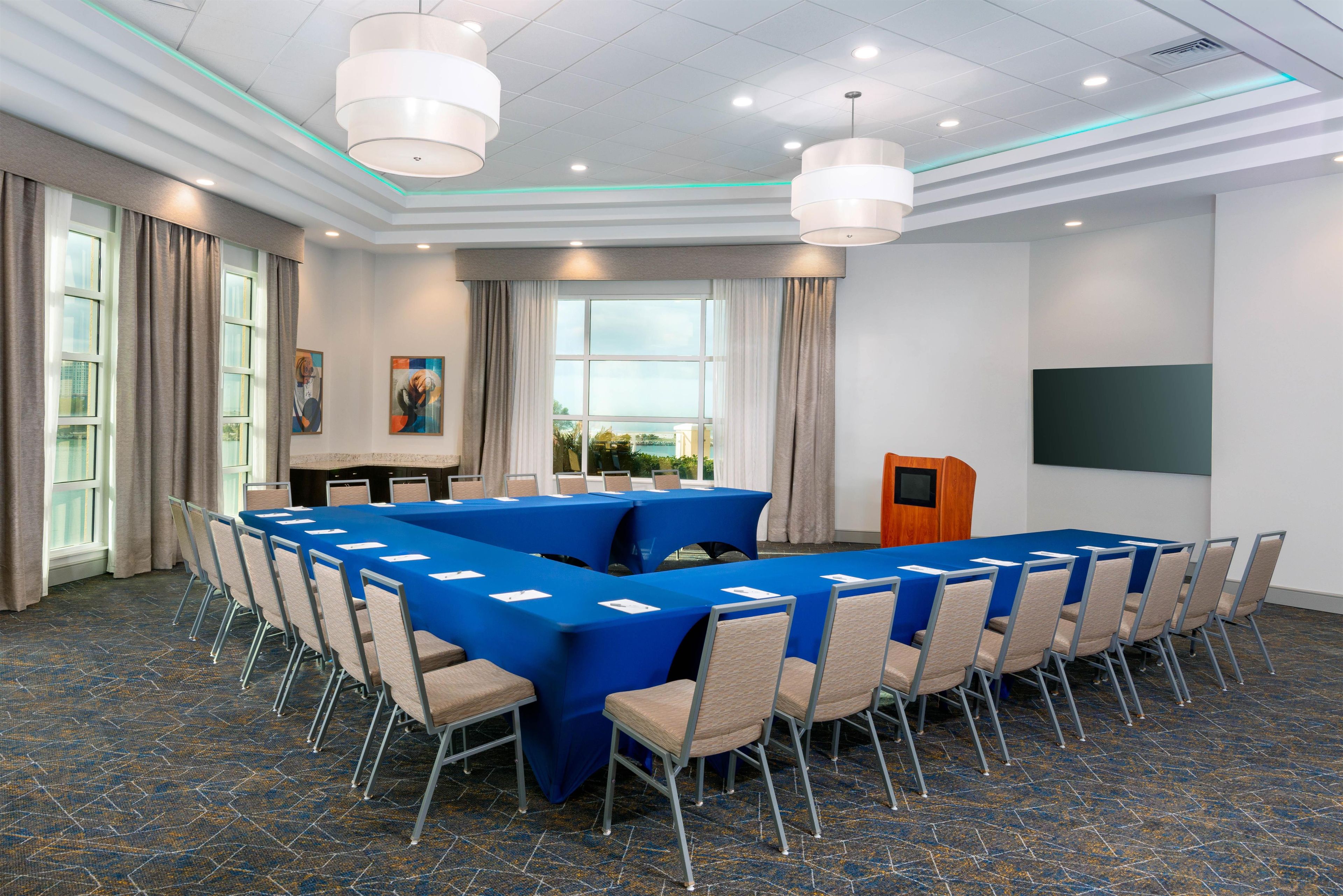 A conference room with a long table, chairs, a podium, and a screen.