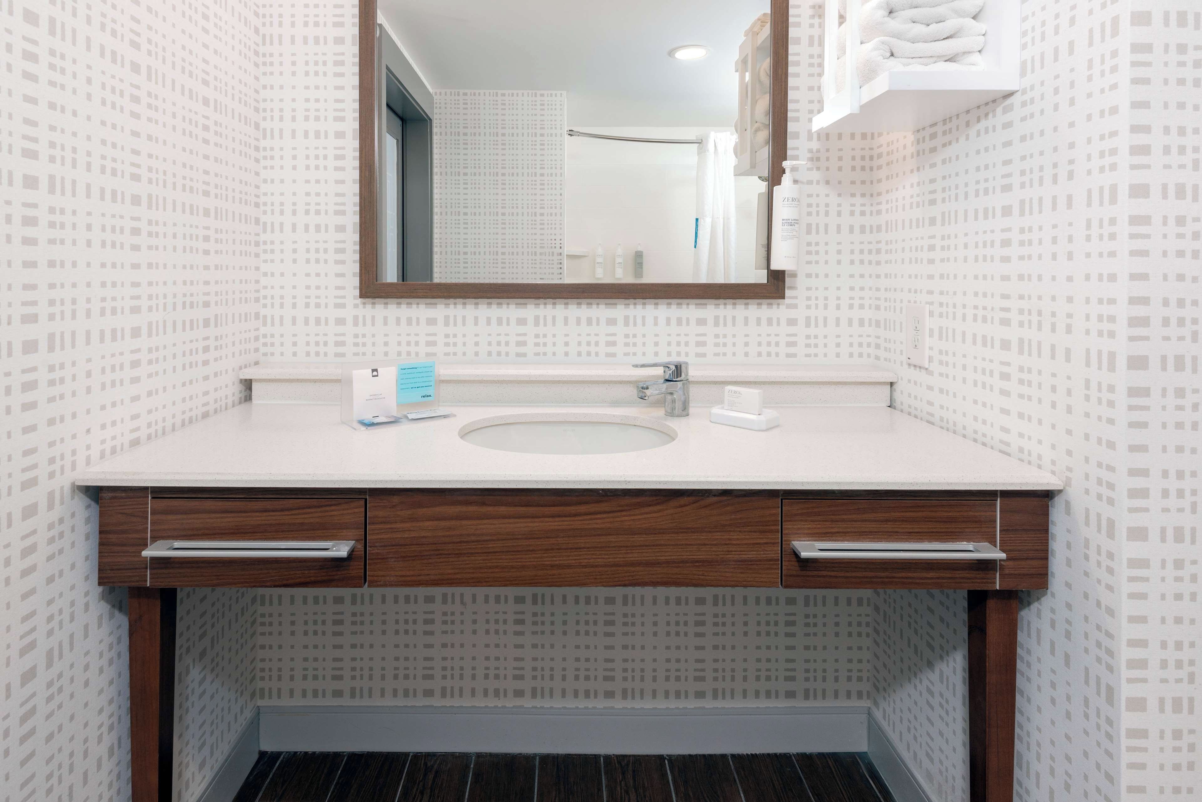A bathroom with a white sink, wooden vanity, and a mirror.