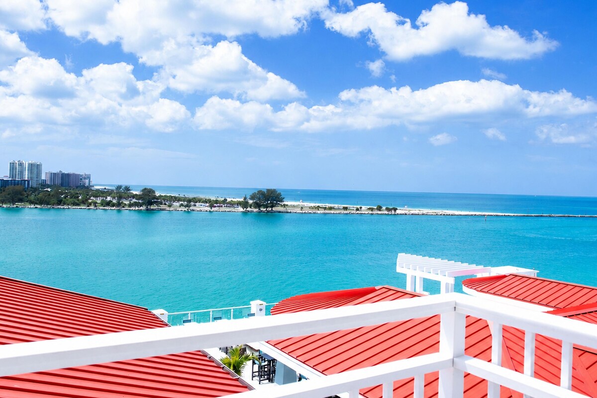A coastal view with a clear sky, a calm sea, and a white building with red roofs.