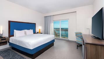 A hotel room with a large bed, a TV, a desk, and a balcony with a view.