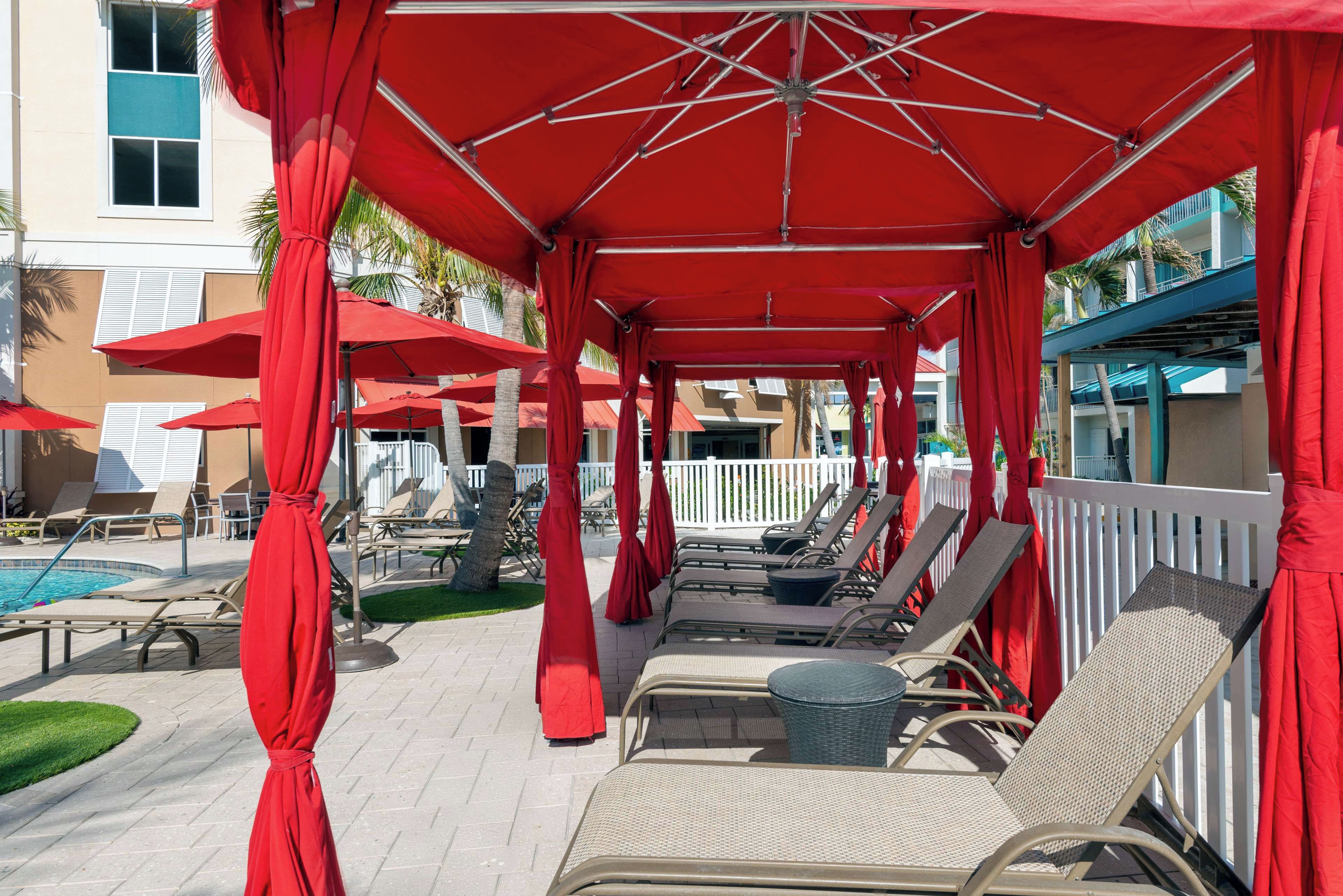 A covered outdoor lounge area with red umbrellas and lounge chairs.
