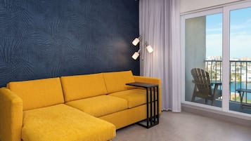 En moderne stue med en gul sofa, et lille sofabord, en gulvlampe og et stort vindue med udsigt til by og pool.