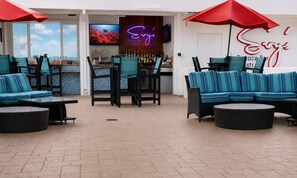 An outdoor seating area with blue-striped sofas and chairs, red umbrellas, and a bar with a neon sign. - Hampton Inn & Suites Clearwater Beach (Clearwater Beach)