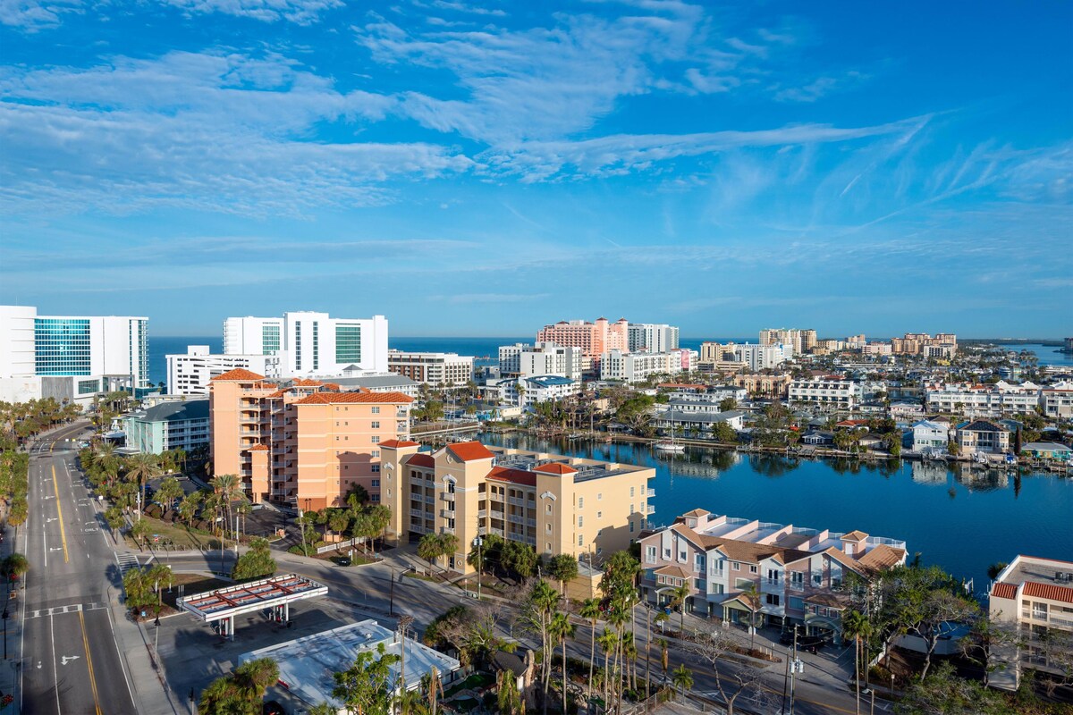 A coastal cityscape with a marina, high-rise buildings, and a clear sky.