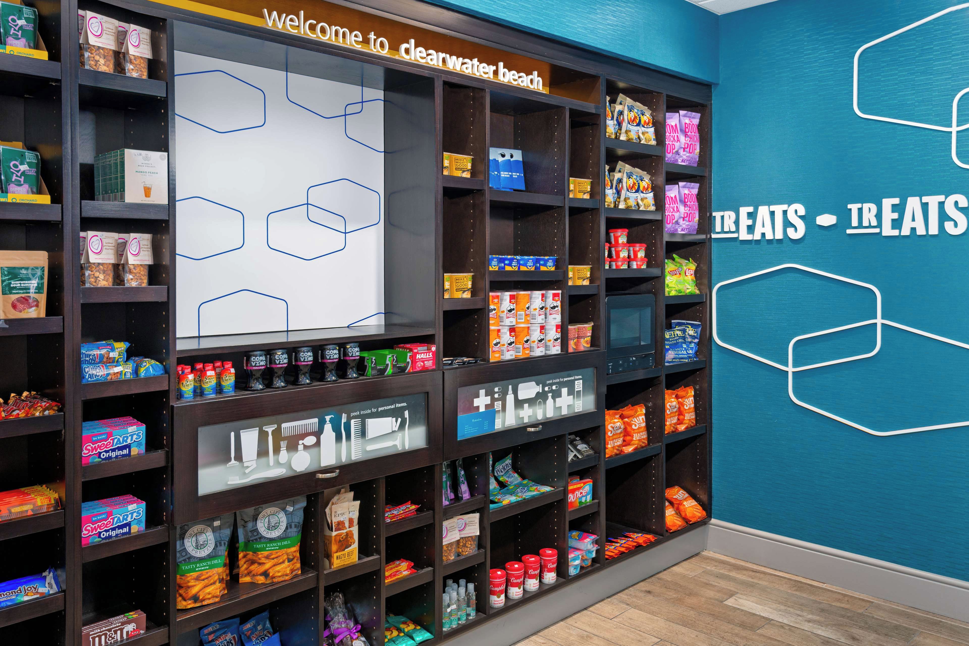 A store with shelves stocked with snacks and beverages, a sign reading 'welcome to Clearwater beach', and a wall with a geometric design.