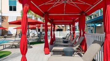 Ein überdachter Außenbereich mit roten Sonnenschirmen, Liegestühlen und einem Pool.