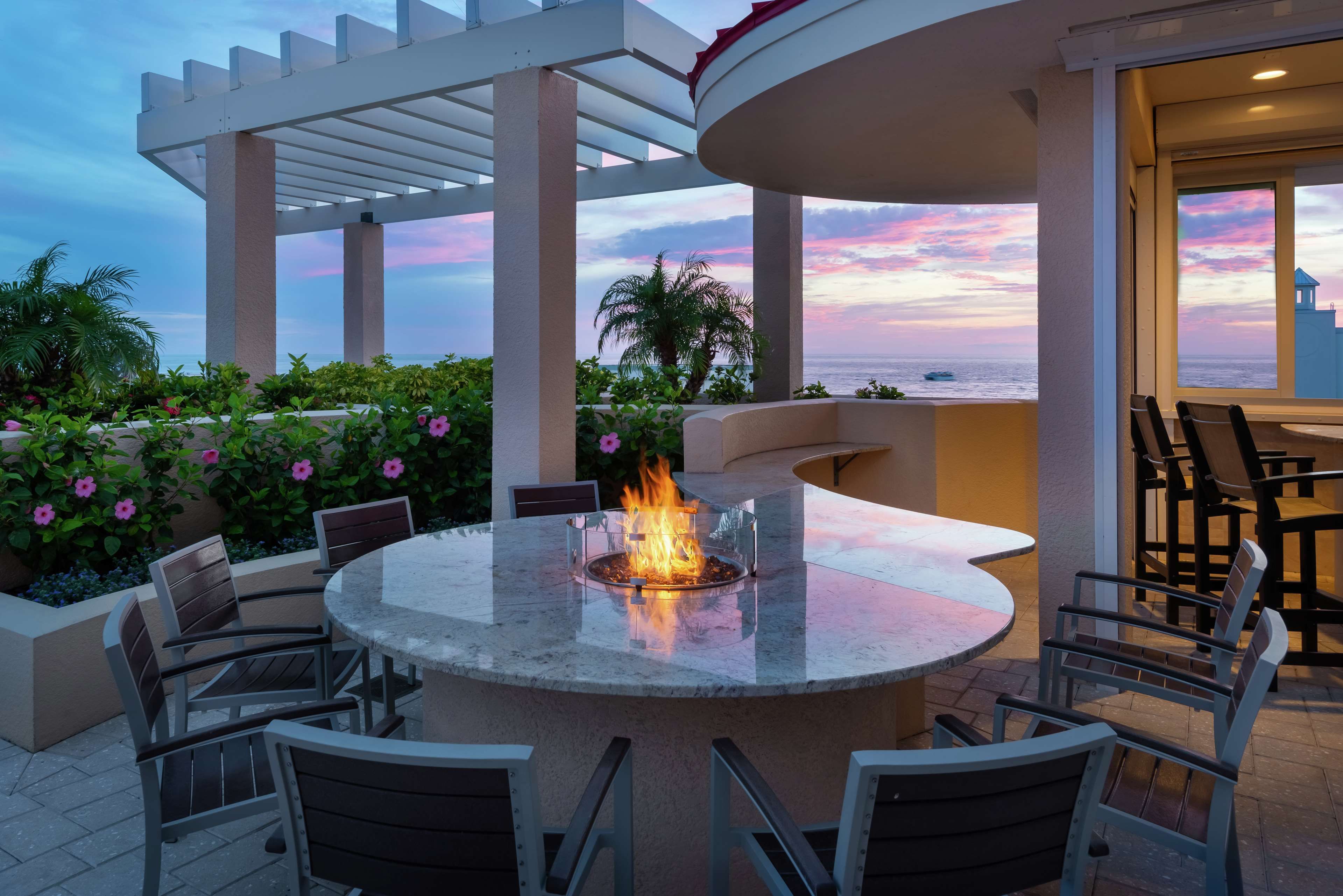 An outdoor patio with a round table and chairs, a fire feature, and a view of the ocean.
