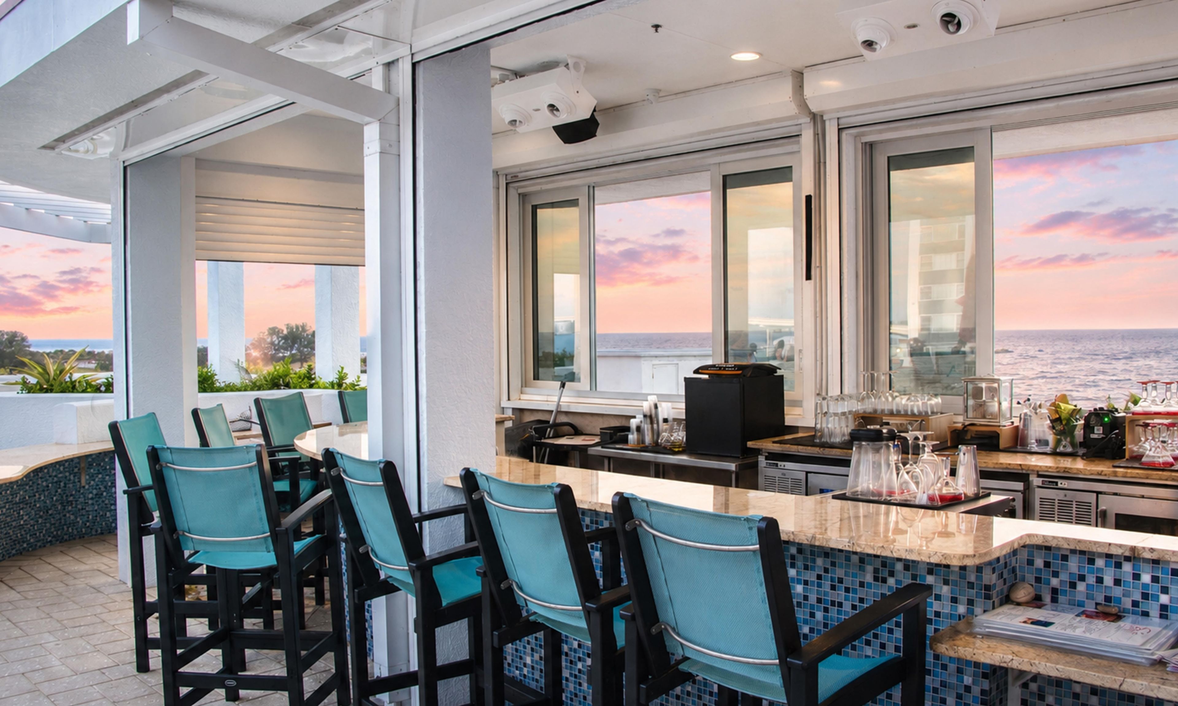 A bar area with a view of the ocean, bar stools, and a coffee machine.