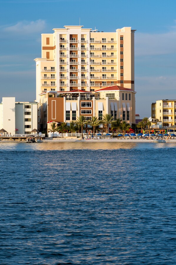 A multi-story hotel with balconies, located near a beach with palm trees and umbrellas. - Hampton Inn & Suites Clearwater Beach (Clearwater Beach)