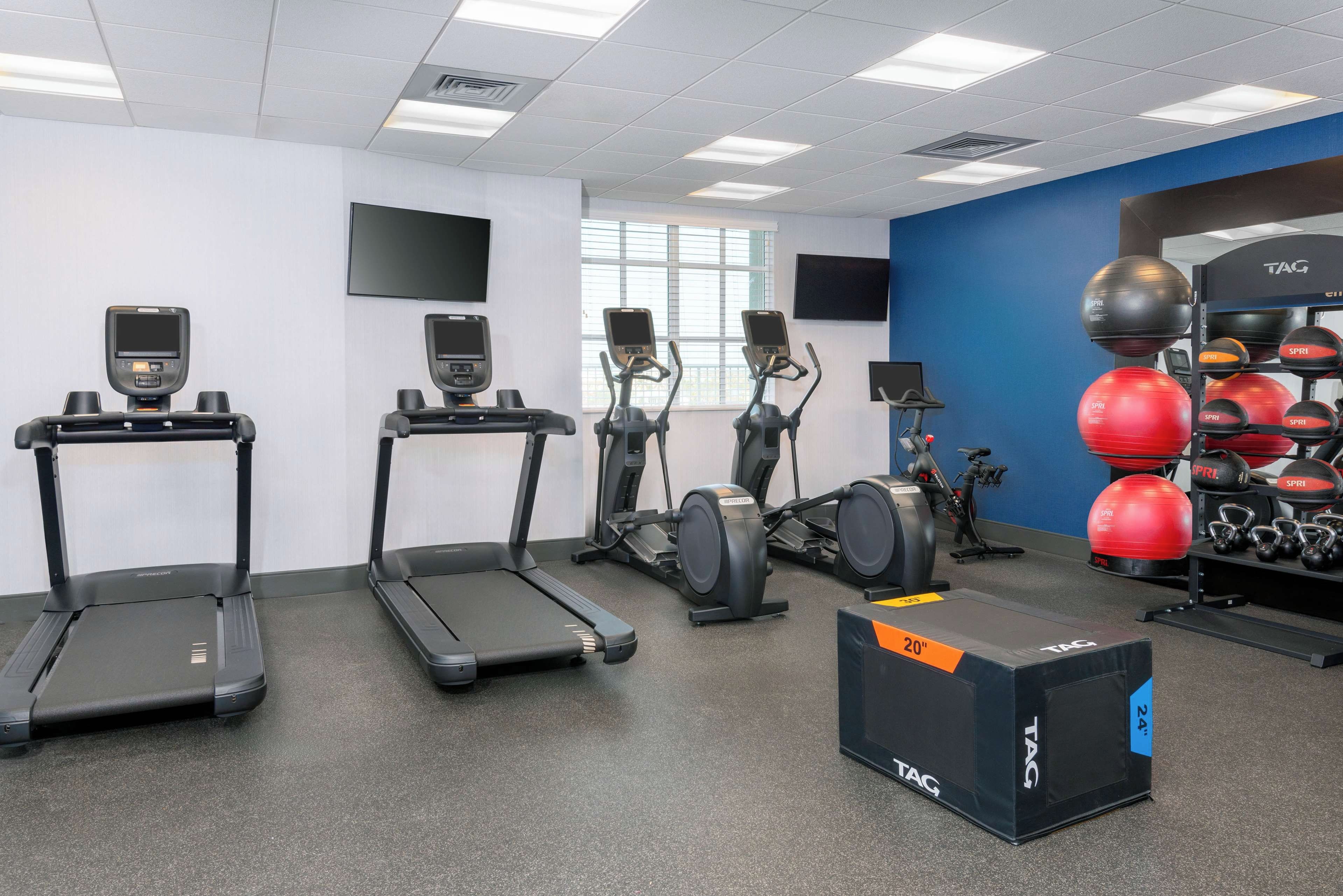 Une salle de sport équipée de tapis de course, de vélos elliptiques et d’un espace dédié à la musculation, avec des kettlebells et des balles lestées.