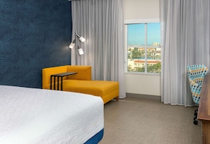 Ein Hotelzimmer mit Bett, gelbem Sessel, kleinem Tisch, Blick auf die Stadt und einer Wand mit Muster.