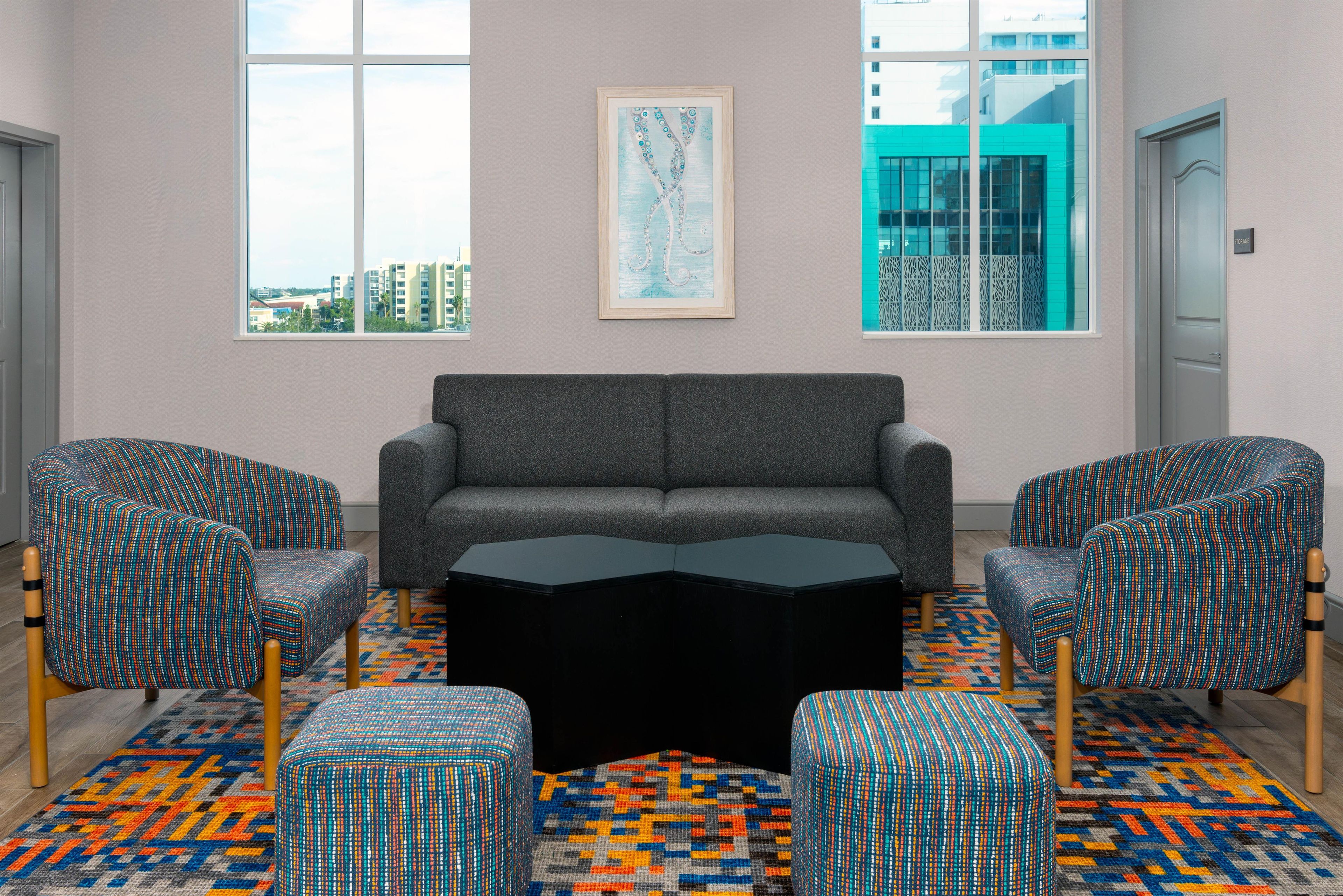 Un espace de détente moderne avec un canapé gris, deux fauteuils à motifs, une table basse noire et un tapis coloré.