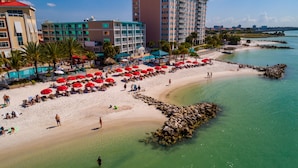 A beach with red umbrellas, a pool, and a view of the city in the background.