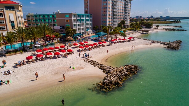 A beach with red umbrellas, a pool, and a view of the city in the background. - Hampton Inn & Suites Clearwater Beach (Clearwater Beach)