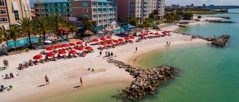 A beach with red umbrellas, a pool, and a view of the city in the background.