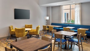 A hotel room with a seating area, tables, and a large window with curtains.