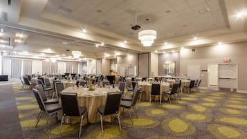 Un amplio salón de banquetes con mesas y sillas redondas, alfombra estampada y un techo alto con iluminación empotrada.