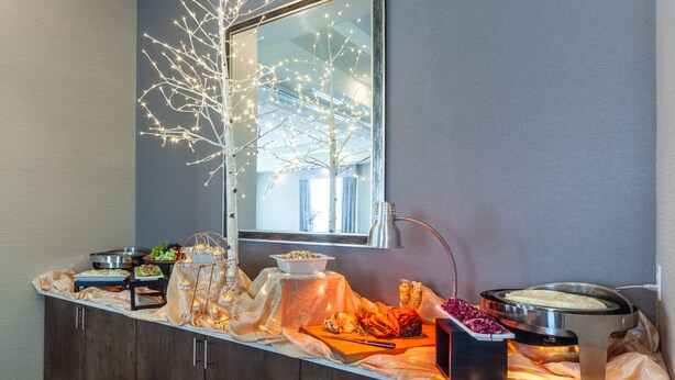 Montaje de bufé con diversos alimentos, un árbol decorativo y una ventana con luz natural.