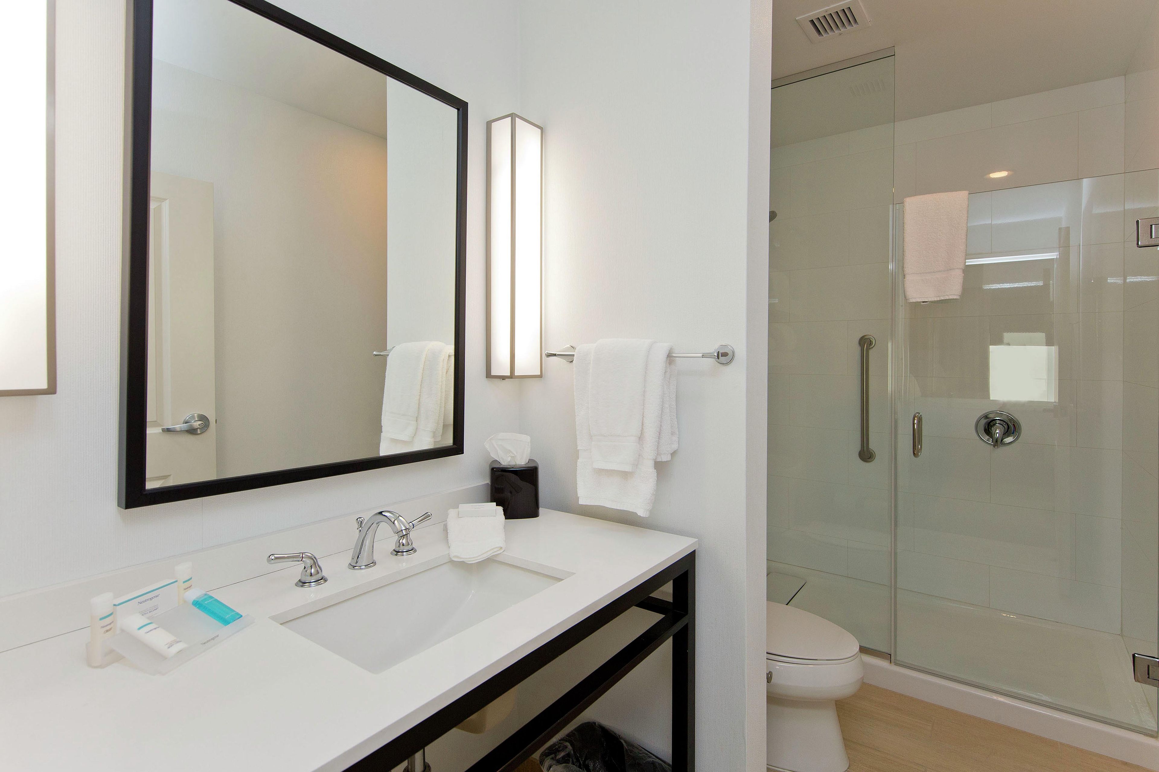 A modern bathroom with a large mirror, a white sink, a toilet, and a glass shower enclosure.