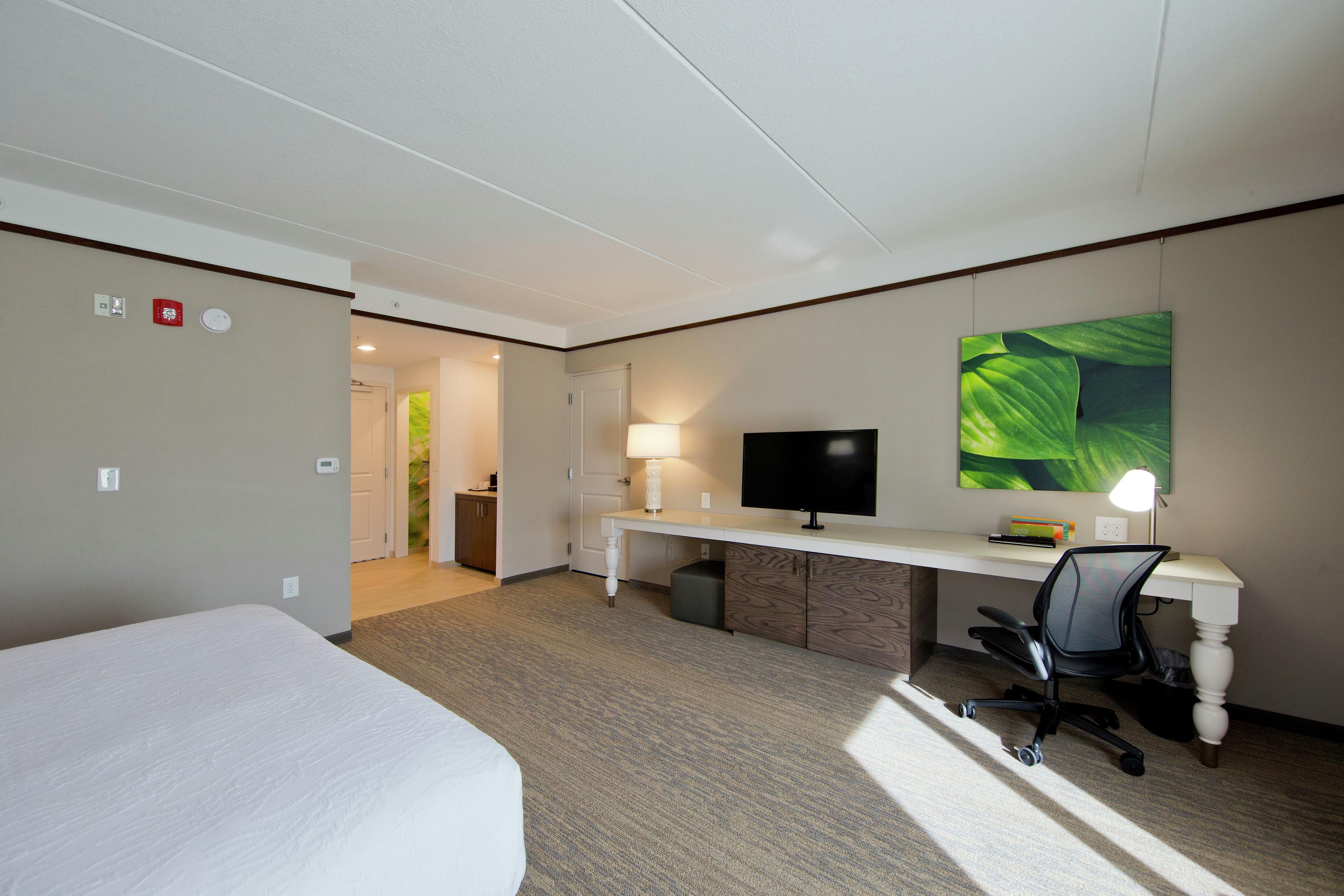 Una habitación de hotel con cama, escritorio, silla, televisor y un cuadro en la pared.