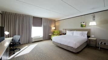 Une chambre d’hôtel avec un lit, un bureau, une chaise, une lampe et un tableau au mur.