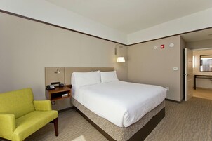 Habitación de hotel con una cama, un sillón verde, una mesita de noche con un teléfono y un escritorio pequeño con una lámpara.