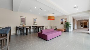 Un vestíbulo amplio con un sofá púrpura, una zona de comedor con sillas y mesas, y una gran planta en maceta.
