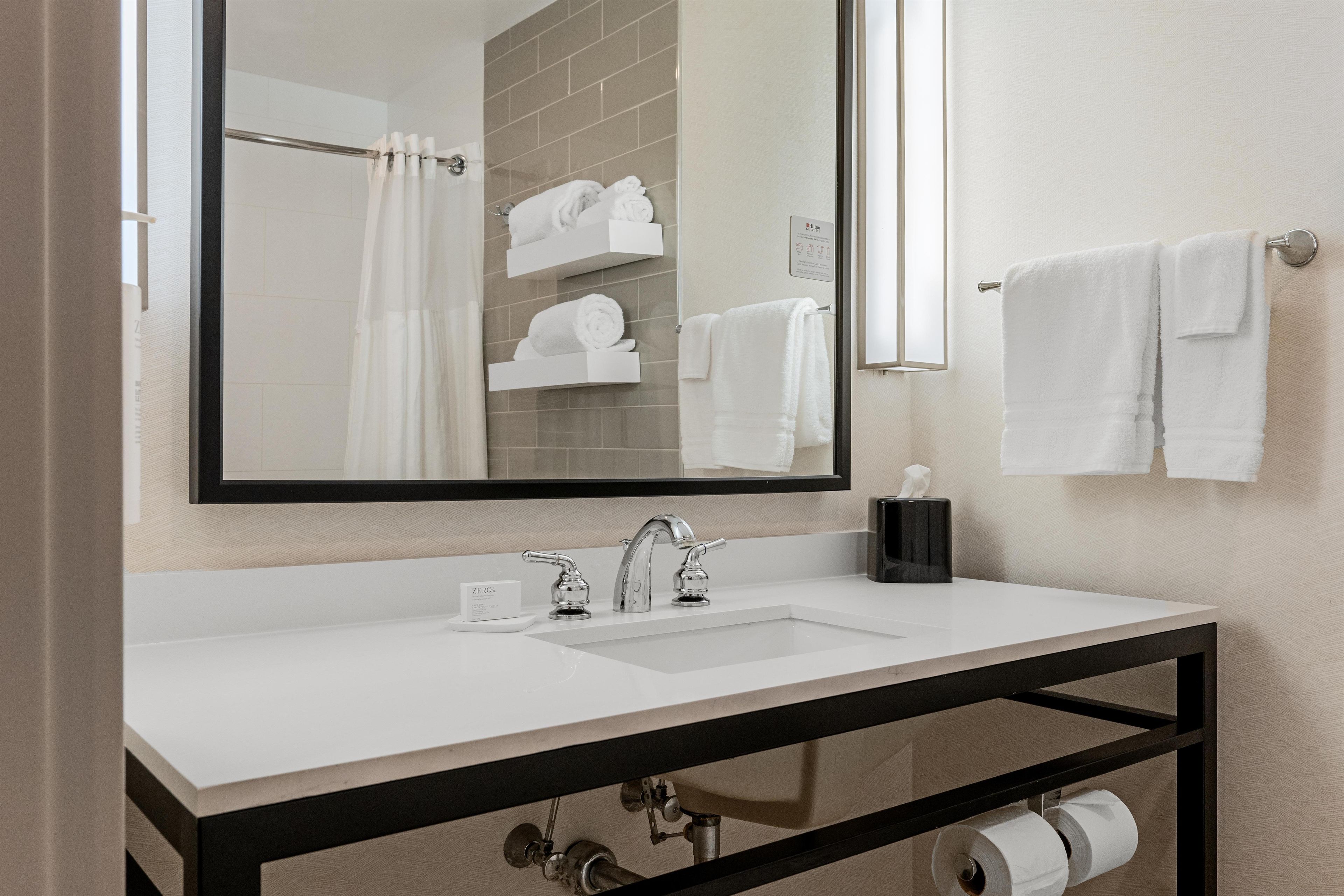 A bathroom with a white sink, a large mirror, and a towel rack with white towels.